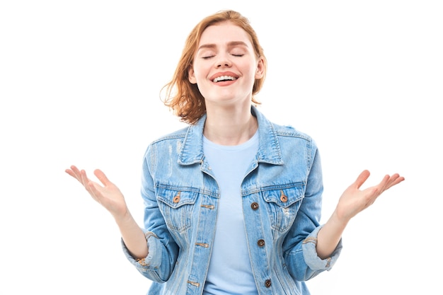 Jeune femme rousse aime regarder la caméra. Jeune fille souriante en jeans sur fond blanc en regardant la caméra. Succès. Écarte ses bras sur les côtés