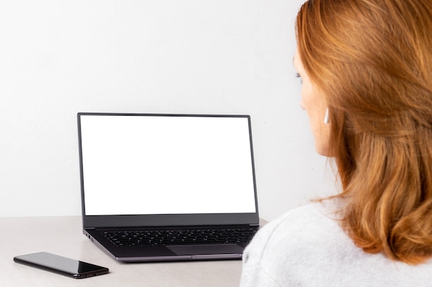 Jeune femme rousse assise devant un ordinateur portable avec une maquette blanche à l'écran