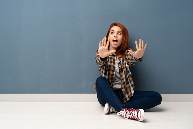 Jeune femme rousse assise sur le sol à compter dix avec les doigts