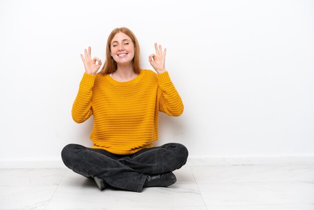 Jeune femme rousse assise sur le sol isolé sur fond blanc dans une pose zen