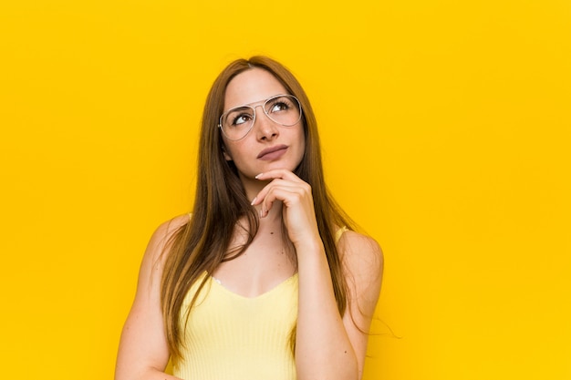 Jeune femme rousse au gingembre avec des taches de rousseur regardant de côté avec une expression sceptique et sceptique.