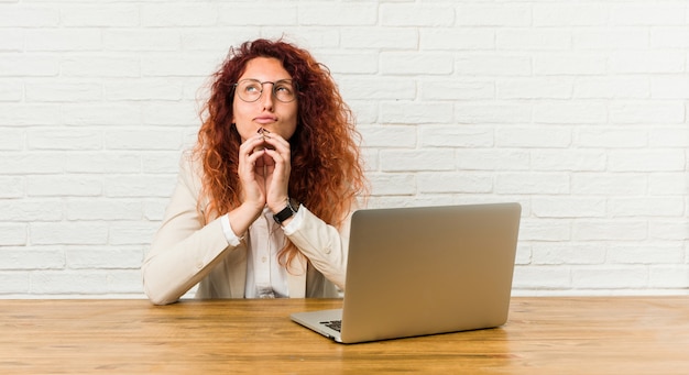 Jeune femme rousse bouclée travaillant avec son ordinateur portable, établissant un plan à l'esprit, mettant en place une idée.