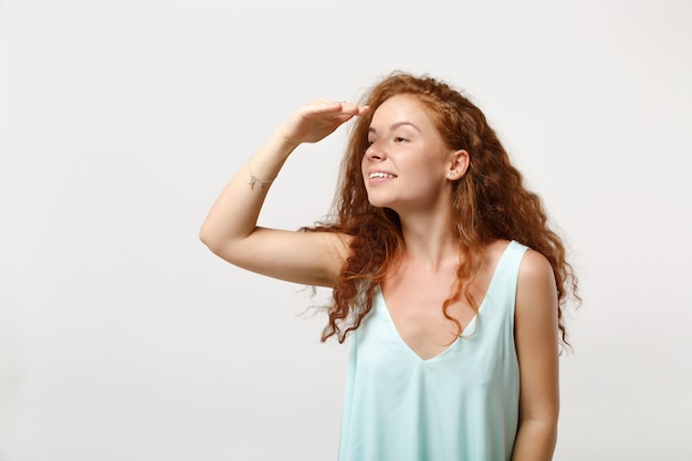 Jeune femme rousse charmante dans des vêtements légers décontractés posant isolé sur fond blanc en studio. Concept de mode de vie des gens. Maquette de l'espace de copie. Tenez la main sur le front en regardant de côté au loin.