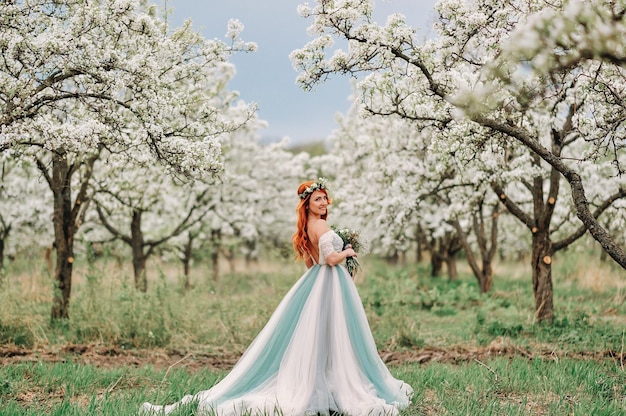 Jeune femme rousse dans une robe luxueuse est debout dans un jardin fleuri