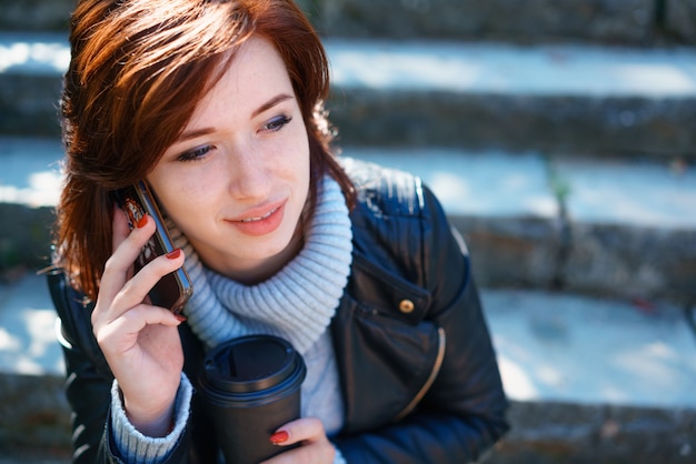 Jeune femme rousse dans une veste en cuir parlant au téléphone à l'extérieur en gros plan