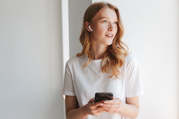 jeune femme rousse écoute de la musique avec des écouteurs par téléphone mobile.