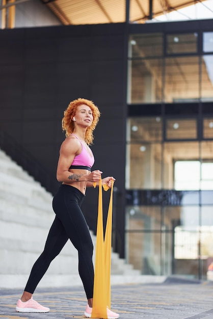 Jeune femme rousse européenne en vêtements sportifs faisant des exercices avec une corde à l'extérieur