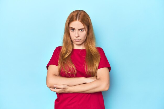 Jeune femme rousse sur fond bleu malheureuse regardant à huis clos avec une expression sarcastique