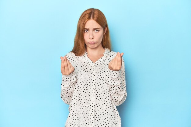 Jeune femme rousse sur fond bleu montrant qu'elle n'a pas d'argent