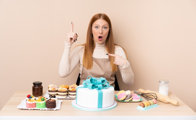 Jeune femme rousse avec un gros gâteau avec une expression faciale surprise