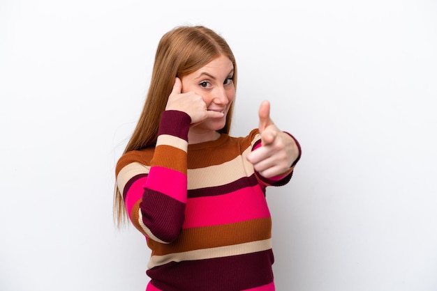 Jeune femme rousse isolée sur fond blanc faisant un geste de téléphone et pointant vers l'avant
