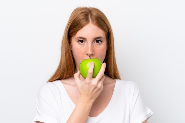 Jeune femme rousse isolée sur fond blanc mangeant une pomme