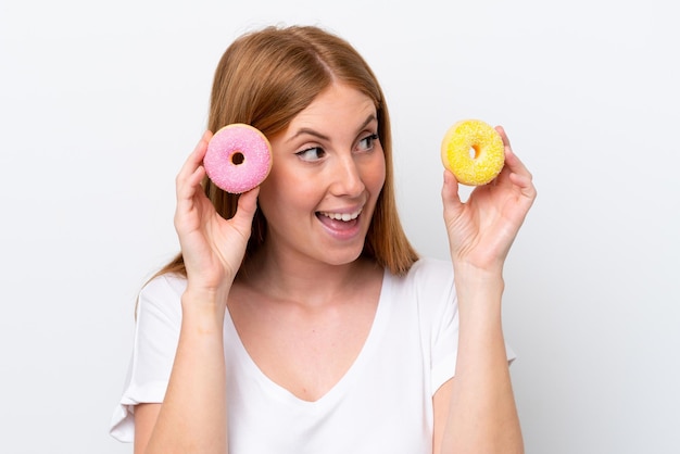 Jeune femme rousse isolée sur fond blanc tenant des beignets et surpris