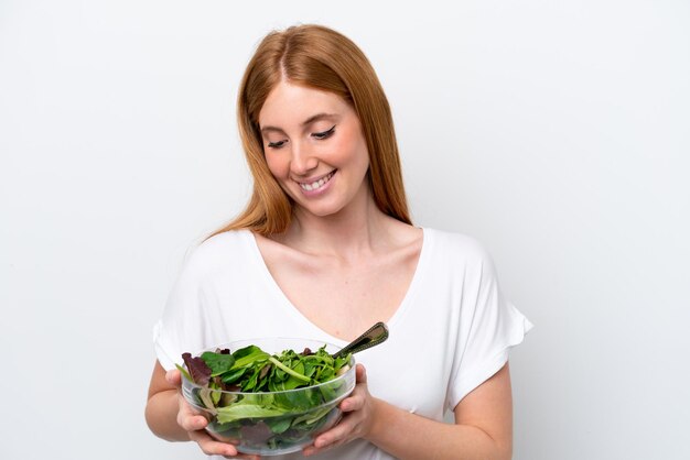 Jeune femme rousse isolée sur fond blanc tenant un bol de salade avec une expression heureuse