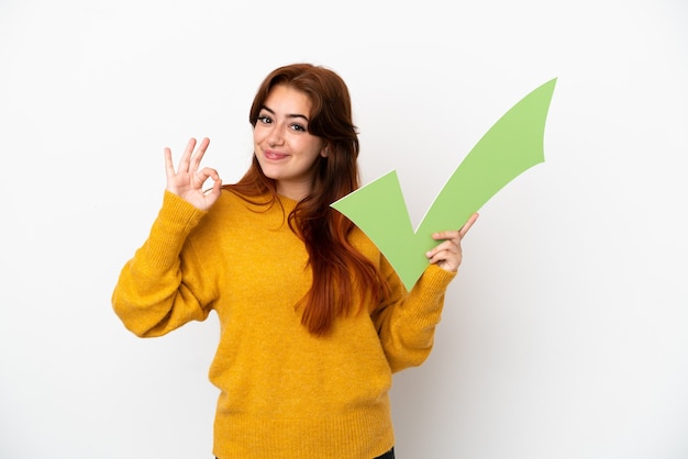 Photo jeune femme rousse isolée sur fond blanc tenant une icône de contrôle et faisant signe ok