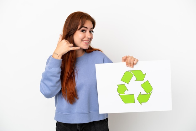 Jeune Femme Rousse Isolée Sur Fond Blanc Tenant Une Pancarte Avec Icône De Recyclage Et Faisant Un Geste De Téléphone