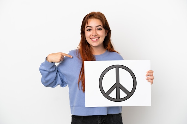 Jeune femme rousse isolée sur fond blanc tenant une pancarte avec le symbole de la paix et le pointant