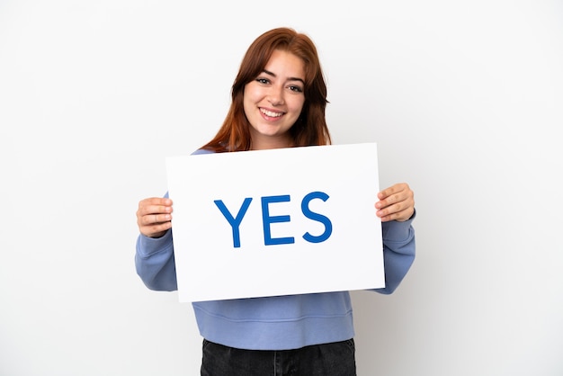 Jeune femme rousse isolée sur fond blanc tenant une pancarte avec texte OUI avec une expression heureuse