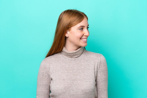 Jeune femme rousse isolée sur fond bleu regardant à côté