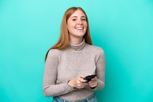 Jeune femme rousse isolée sur fond bleu surprise et envoyant un message