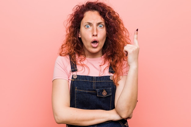 Jeune femme rousse jolie gingembre portant une salopette jeans ayant une excellente idée, concept de créativité.