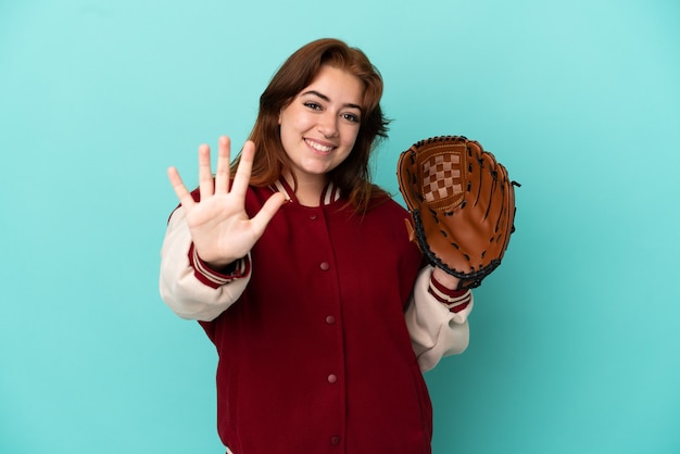 Jeune femme rousse jouant au baseball isolé sur fond bleu comptant cinq avec les doigts