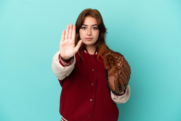 Jeune femme rousse jouant au baseball isolé sur fond bleu faisant un geste d'arrêt