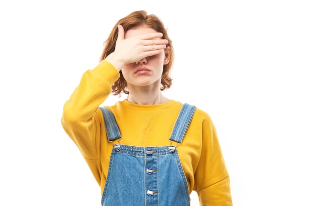 Jeune femme rousse lorgnant à travers les doigts couvrant les yeux avec des paumes isolé sur fond blanc Phobia Concept