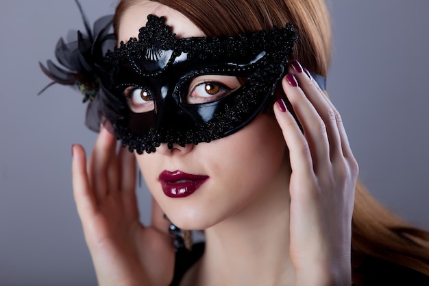 Jeune femme rousse en masque de carnaval sur fond gris