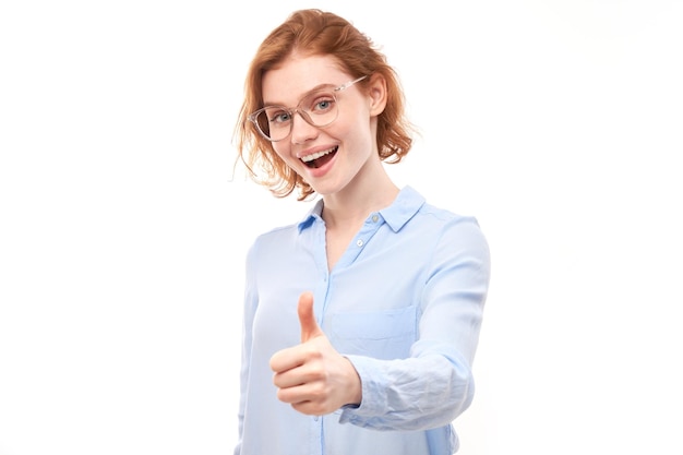 Jeune femme rousse montre la main avec les pouces vers le haut et sourit à la caméra isolée sur fond blanc