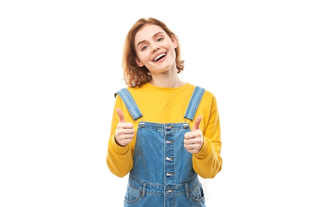 Jeune femme rousse montre la main avec les pouces vers le haut et sourit à la caméra isolée sur fond blanc