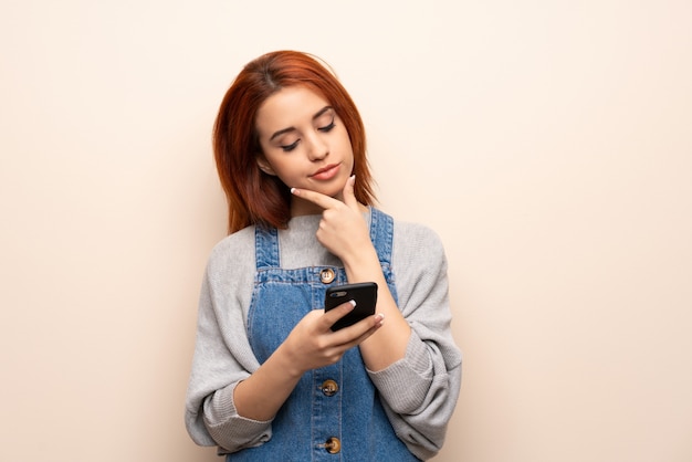 Jeune femme rousse sur mur isolé célébrant une victoire avec un téléphone portable