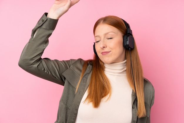 Jeune femme rousse sur mur rose isolé écouter de la musique et de la danse