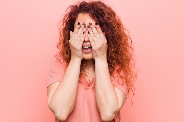 Une jeune femme rousse naturelle et authentique couvre les yeux avec les mains, un large sourire attendait une surprise.