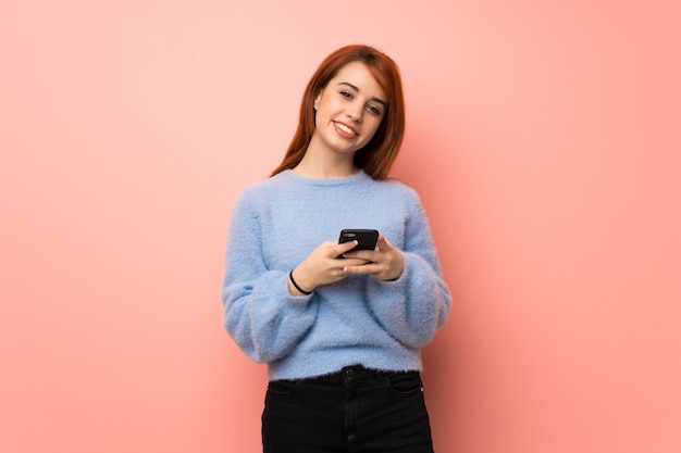 Jeune femme rousse sur rose envoyant un message avec le téléphone portable