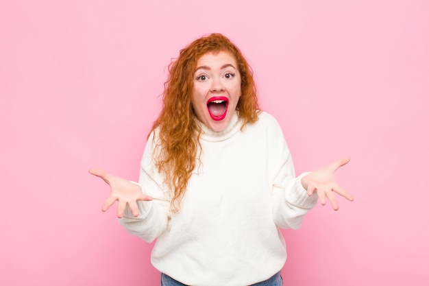 Jeune femme rousse se sentant heureuse, étonnée, chanceuse et surprise, comme dire sérieusement omg? Incroyable sur un mur rose