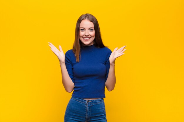 Jeune femme rousse se sentant heureuse, excitée, surprise ou choquée, souriante et étonnée de quelque chose d'incroyable contre un mur plat