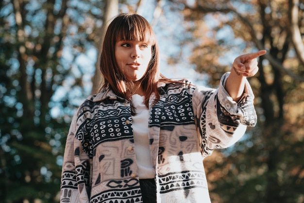 Jeune femme rousse sinueuse surprise et pointant quelque chose à l'extérieur avec espace de copie. Notion de carte postale. Annonce et publicité. Agite sa main, saluant.