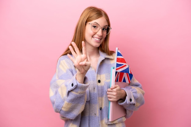 Jeune femme rousse tenant un drapeau du Royaume-Uni isolé sur fond rose heureux et comptant quatre avec les doigts