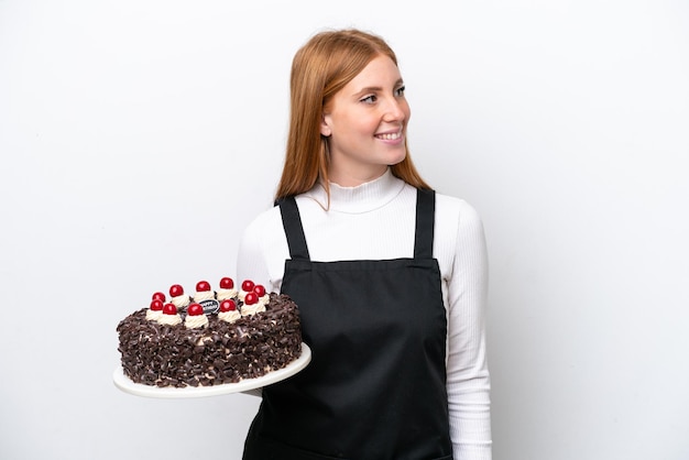 Jeune femme rousse tenant un gâteau d'anniversaire isolé sur fond blanc à côté