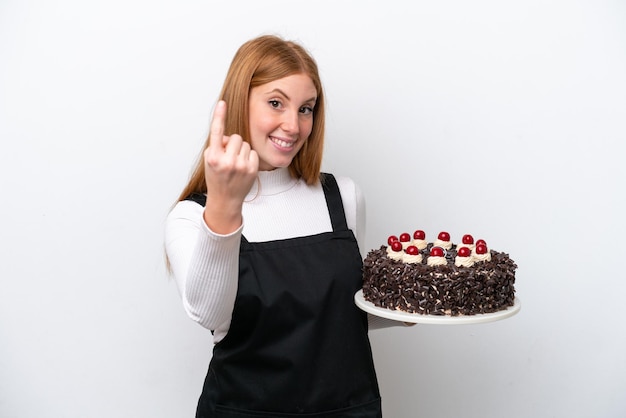 Jeune femme rousse tenant un gâteau d'anniversaire isolé sur fond blanc faisant un geste à venir