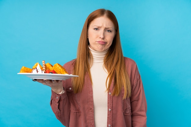 Jeune femme rousse tenant des gaufres avec une expression triste