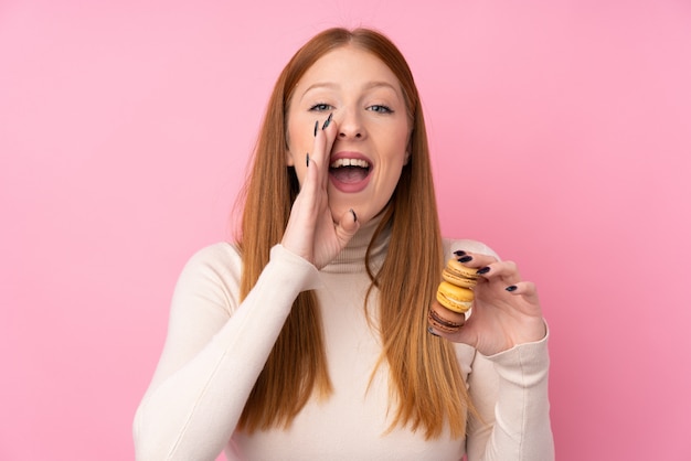 Jeune femme rousse tenant des macarons français colorés et criant