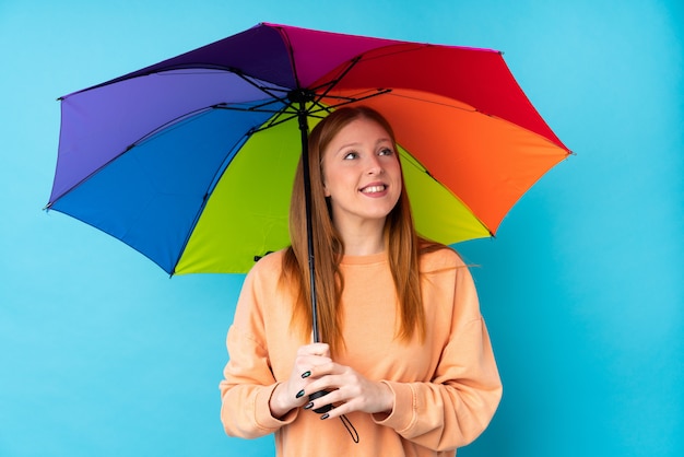 Jeune femme rousse tenant un parapluie sur un mur isolé en levant tout en souriant