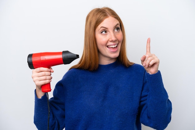 Jeune femme rousse tenant un sèche-cheveux isolé sur fond blanc dans l'intention de réaliser la solution tout en levant un doigt