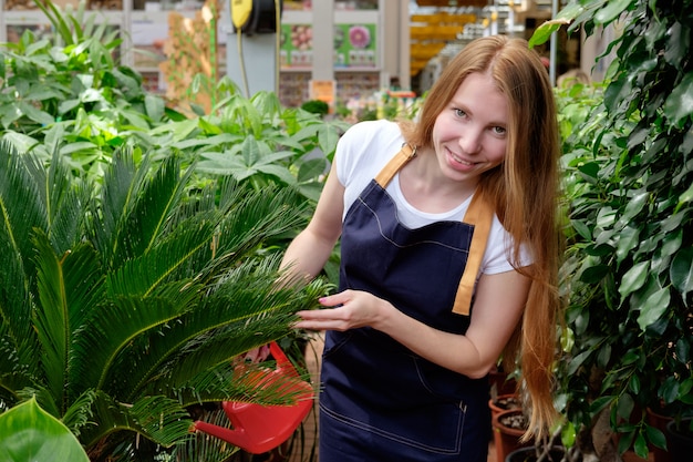 Jeune femme rousse travailleur en serre de marché aux plantes versant des plantes et souriant