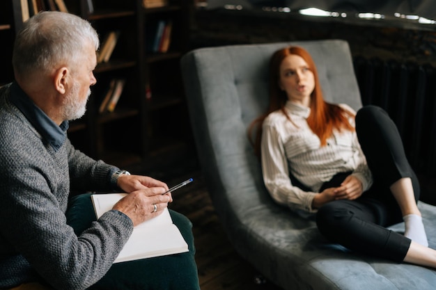 Une jeune femme rousse triste allongée sur un canapé parle à un psychologue homme mûr