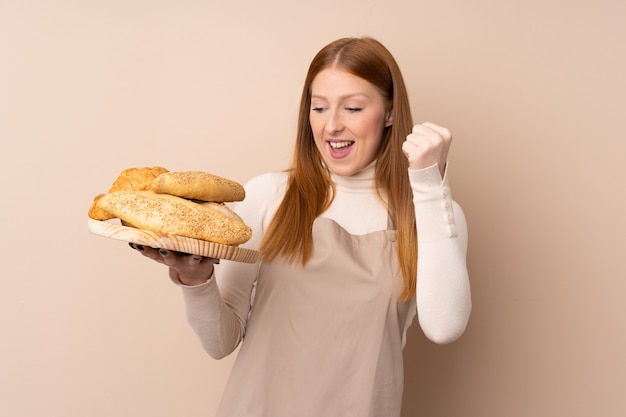 Jeune femme rousse en uniforme de chef. Boulanger tenant une table avec plusieurs pains célébrant une victoire