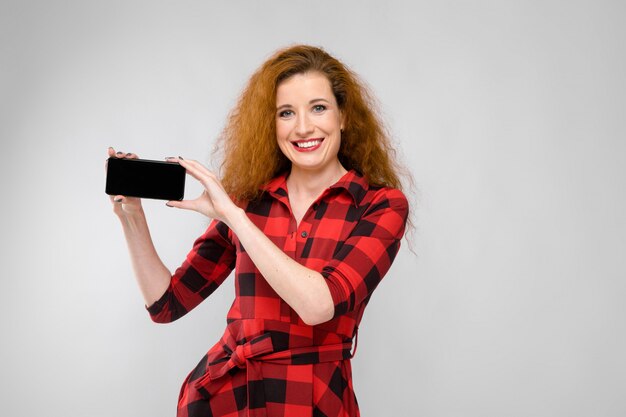 Jeune femme rousse vêtue d'une chemise à carreaux rouge. jeune femme tenant un téléphone