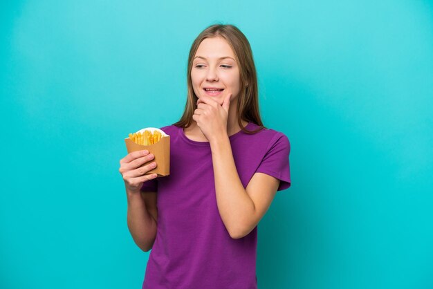 Jeune femme russe attrapant des frites isolées sur fond bleu regardant sur le côté et souriant